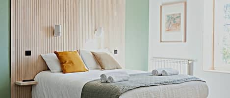 Un dormitorio moderno con un cabecero de listones de madera, una cama con colcha gris y blanca, y suelo de madera.