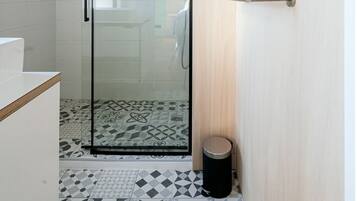 Une salle de bain moderne avec une porte de douche en verre, des carreaux de sol à motifs et une porte en bois dotée d’un porte-serviettes.