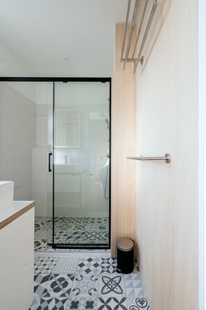 A modern bathroom with a glass shower door, patterned floor tiles, and a wooden door with a towel rack. - Olive Green Room (Nîmes)