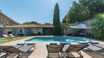 Un espace piscine avec des chaises longues et, en arrière-plan, un bâtiment en pierre.