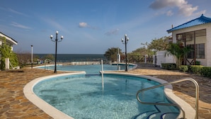 Una piscina con agua azul cristalina, rodeada de baldosas de piedra y equipada con barandales de metal.