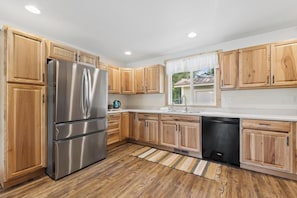 A kitchen with wooden cabinets, stainless steel appliances, a dishwasher, and a window with a view.