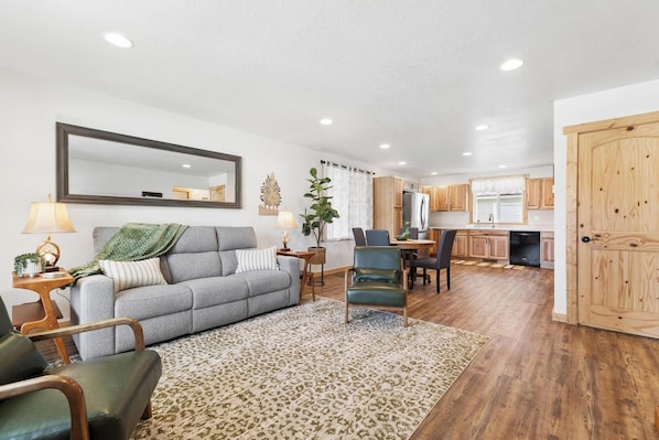 A living room with a sofa, a chair, a dining table, and a kitchen in the background.