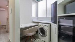 A laundry room with a washing machine, a chair, and a large window. - Full Studio in Floripa Smu0201 (Florianópolis)