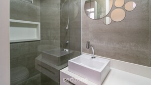 A modern bathroom with a glass-enclosed shower, a white sink, and a decorative mirror with circular elements. - Full Studio in Floripa Smu0201 (Florianópolis)