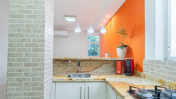 A kitchen with a granite countertop, a sink, and a gas stove. There are three pendant lights, a potted plant, and a window with a view of trees. - Full Studio in Floripa Smu0201 (Florianópolis)