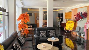 A modern hotel lobby with a black leather sofa, a round wooden table, and a dining area with a black table. - Bumi Geulis Hotel & Residence (Sukabumi)