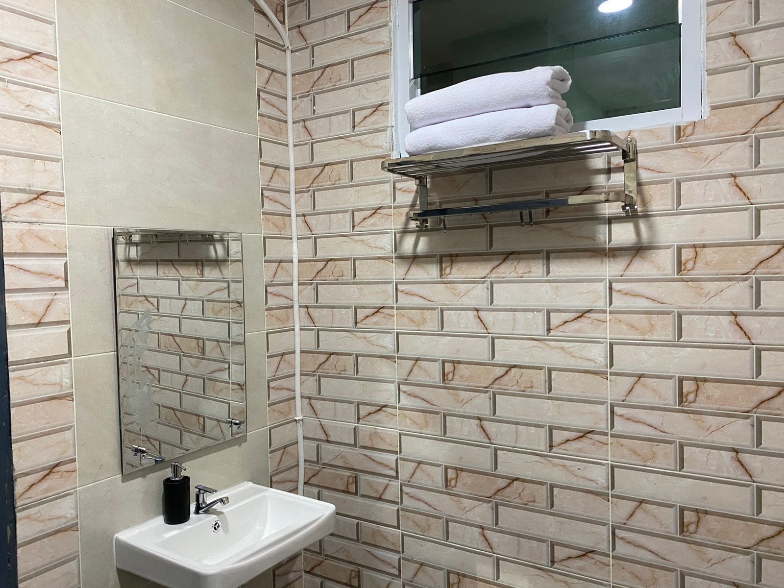 Une salle de bain avec un mur recouvert de carreaux de marbre, un lavabo, un miroir et un porte-serviettes.
