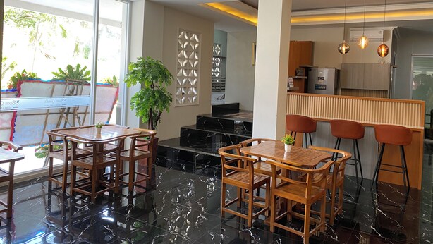 A modern dining area with wooden furniture and a glass table, a kitchen with wooden cabinets and bar stools, and a decorative wall panel. - Bumi Geulis Hotel & Residence (Sukabumi)