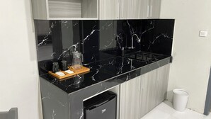 A modern kitchen with a black marble countertop, a built-in oven, and a small refrigerator. - Bumi Geulis Hotel & Residence (Sukabumi)