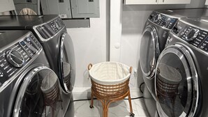 A laundry area with two front-loading washing machines, a wicker laundry basket, and a white tiled floor. -  Spacious 3BR 2BA Apt Near JFK (Jamaica)