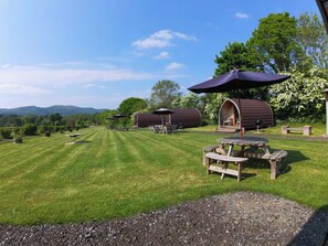 Un espace extérieur verdoyant avec des tables de pique-nique, des parasols et des structures en bois.