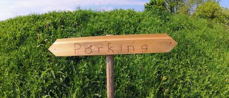 Un panneau en bois sur lequel est écrit le mot « Parking », placé devant un décor de verdure luxuriante composé de gazon et d’arbres.