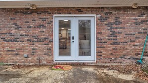 A brick exterior wall with a white-framed glass door, a doormat, and a broom leaning against the wall.