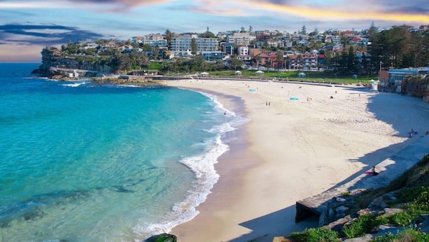 Una platja costanera amb aigües turqueses cristal·lines, sorra daurada i edificis residencials al fons.