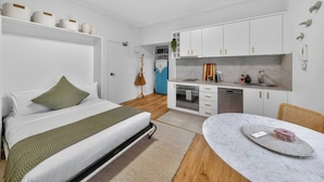 Habitació moderna i compacta amb llit, taula rodona petita, cuineta i bany.