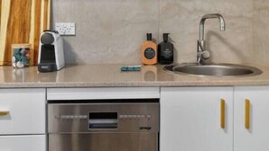 Una cuina moderna amb armaris blancs, un rentaplats d'acer inoxidable, una taula de tall de fusta, una cafetera i dues ampolles de sabó per mans.