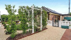 En trädgård med en pergola, en byggnad i tegel med en grind som leder in, och en grusgång.