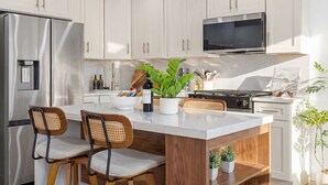 A modern kitchen with white cabinets, stainless steel appliances, a central island with seating, and a flat-screen TV above the stove. - Modern 3BR • Near Downtown Boston • Walk to T • Minutes to Logan • Free Parking (Boston)