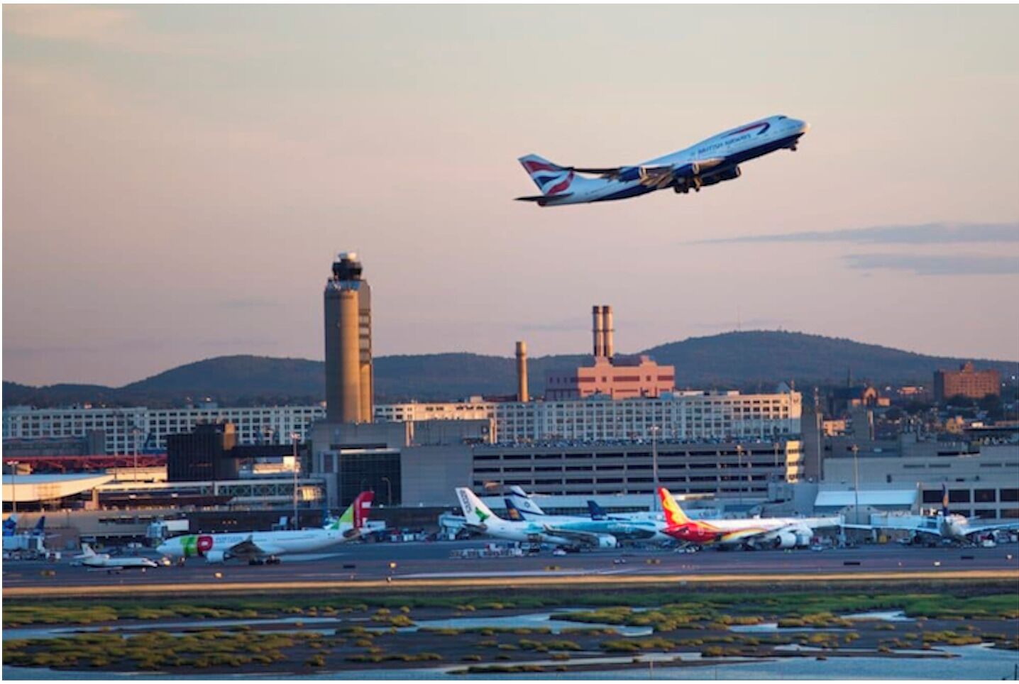 Ein Flugzeug startet vom Flughafen, im Hintergrund sind mehrere Terminals und Hangars zu sehen.