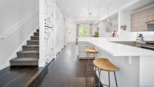 A modern kitchen with a central island, bar stools, and a staircase with a decorative railing. - The Sage Sanctuary: A Sensory Friendly 4BR Retreat in the Heart of Denver (Denver)