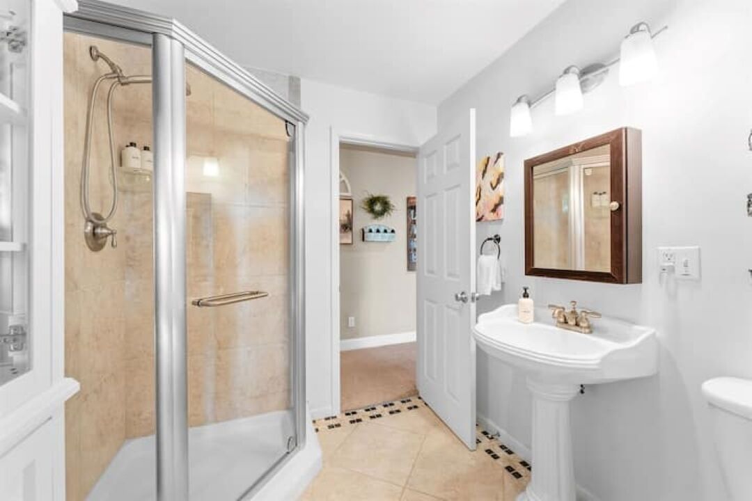 A bathroom with a glass shower enclosure, a pedestal sink, and a mirror above the sink.