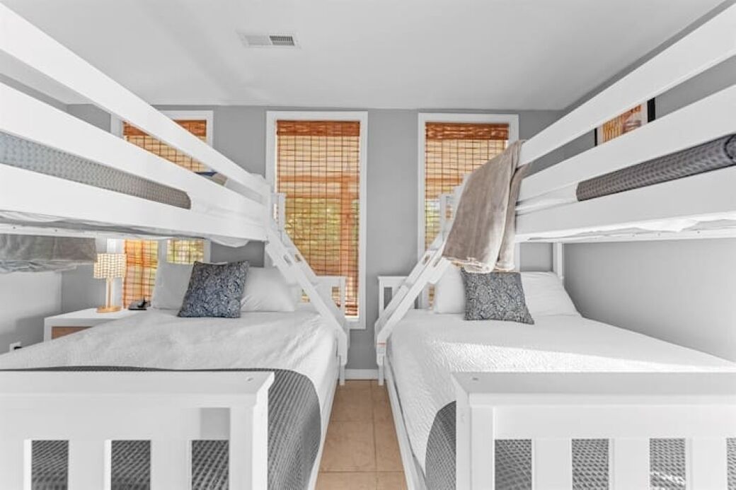 Une chambre avec des lits superposés, une petite table de chevet avec une lampe et une fenêtre avec des stores.