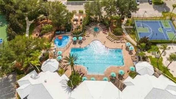 Une grande piscine extérieure entourée de chaises longues et de parasols, avec un terrain de basketball en arrière-plan.