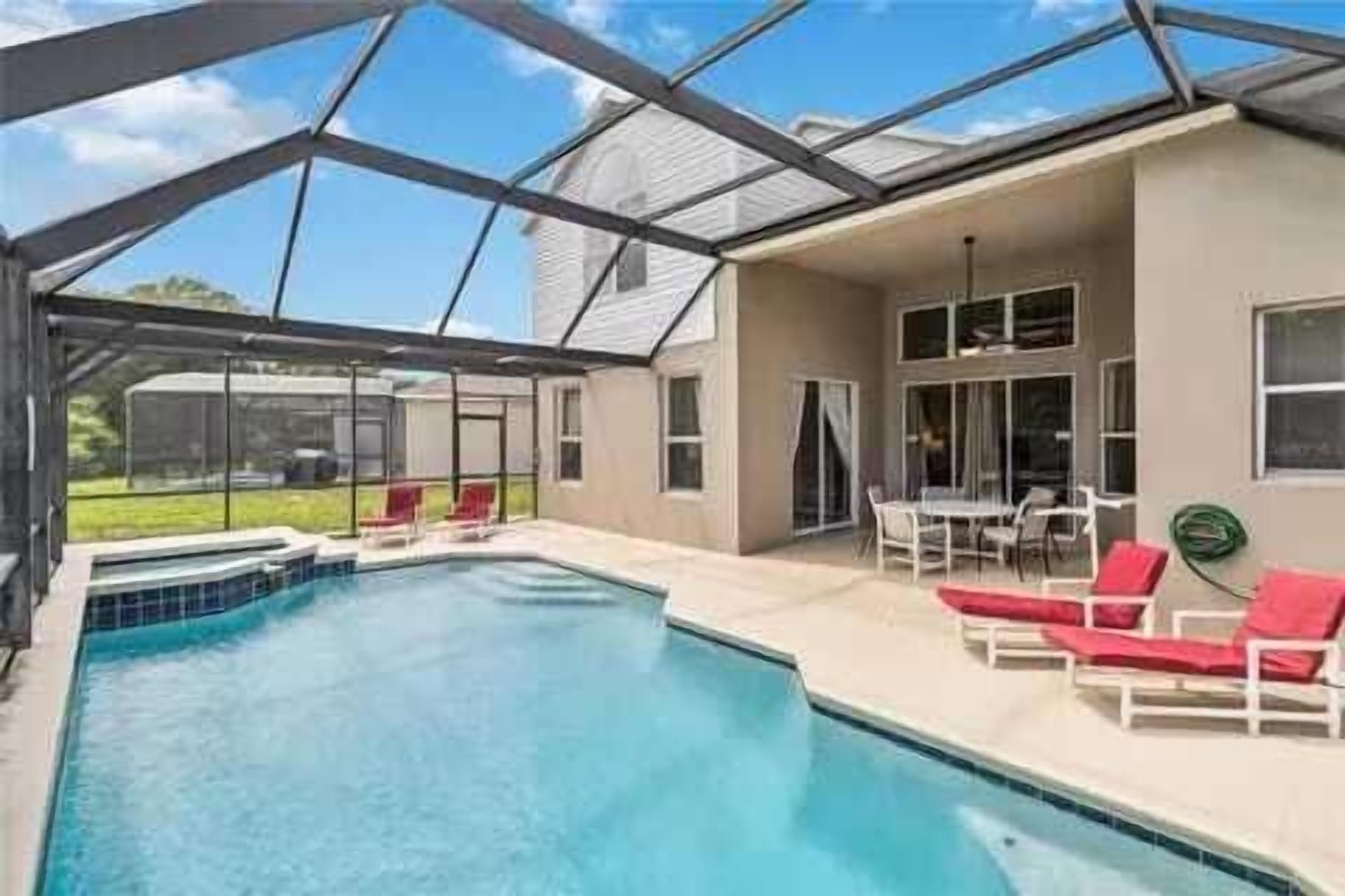 A covered outdoor swimming pool with a glass roof, surrounded by lounge chairs and a table.