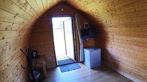 Habitació acollidora amb panells de fusta, sostre inclinat, nevera petita, televisió penjada a la paret i una porta que dona a l'exterior.