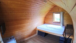 Una habitació petita amb panells de fusta, un llit individual, una finestra i una televisió.