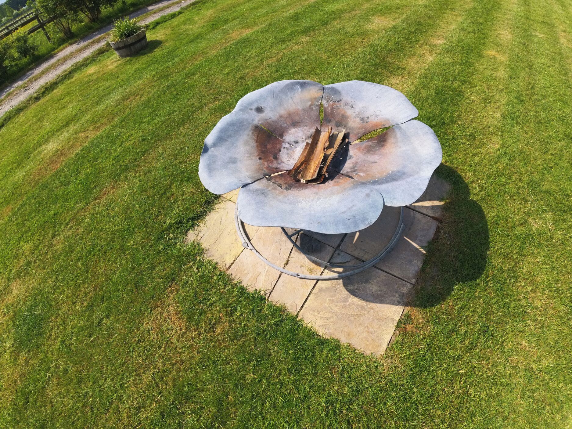 A metal fire pit with a flower-like design, surrounded by a stone base, set in a grassy outdoor area.