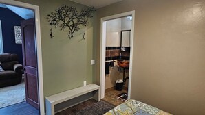 Ein Schlafzimmer mit einem Bett, einer Bank, einer Wanddekoration und Blick zur Küche.