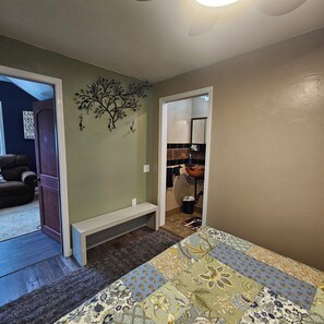 A bedroom with a bed, a bench, a decorative wall piece, and a view into the kitchen. - Beautiful Lake Frontage house, handicap friendly, on Long Lake, Dundee Wisconsin (Campbellsport)