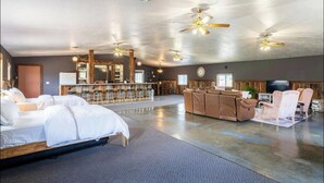 Ruime hotelkamer met een groot bed, een zithoek met een bank en stoelen, een bar met krukken, en een televisie.