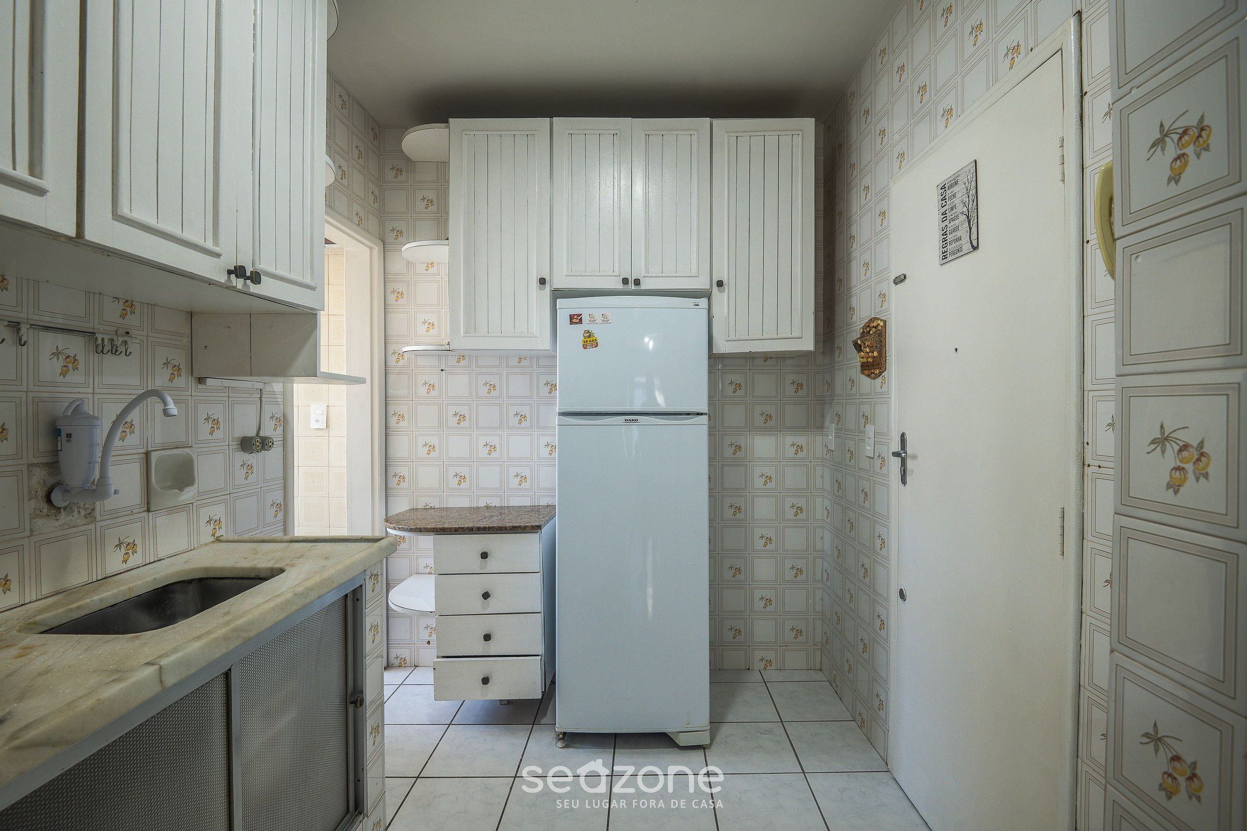 A compact kitchen with white cabinets, a built-in sink, and a refrigerator.