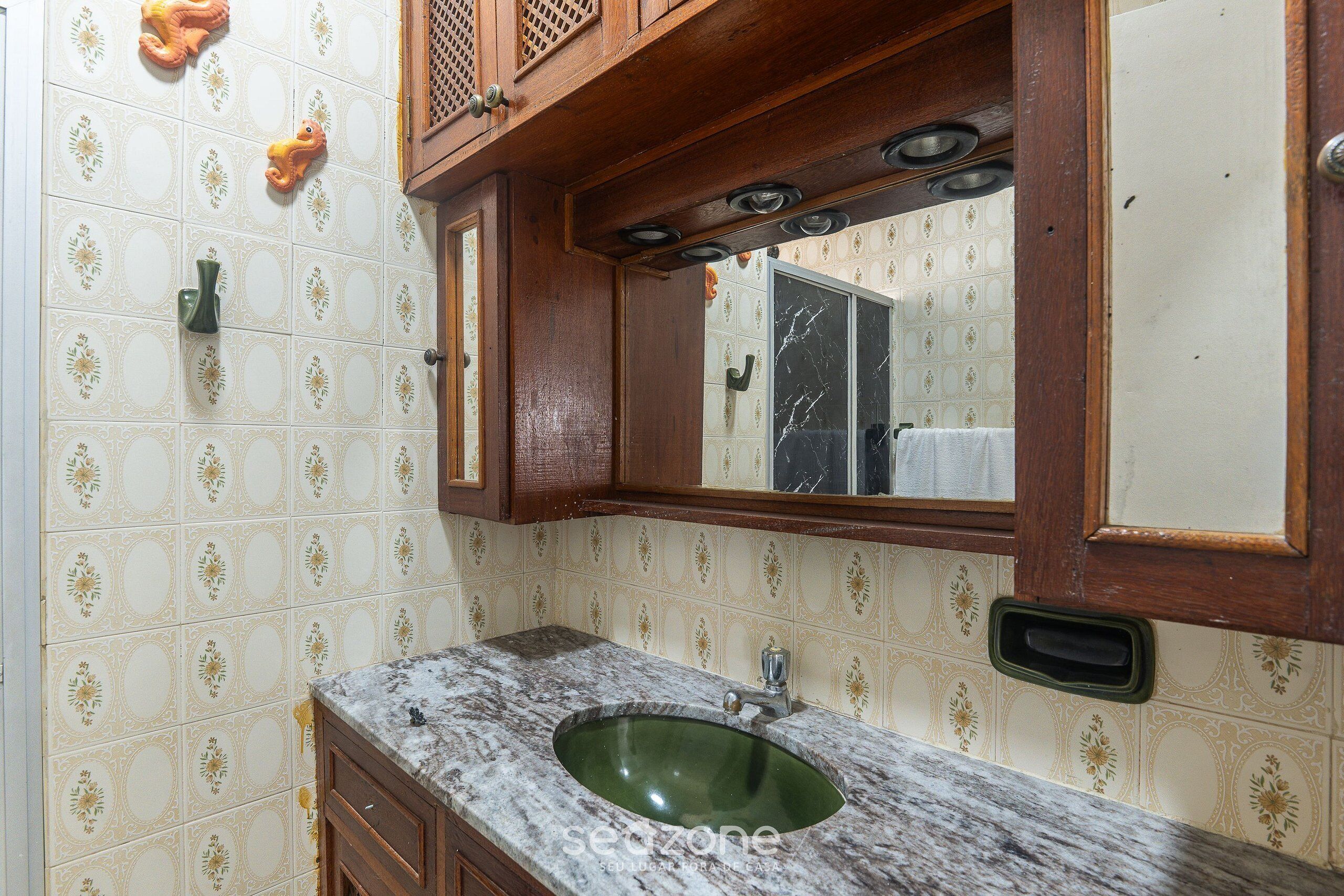 Un baño con lavamanos de mármol, armarios de madera y baldosas estampadas.