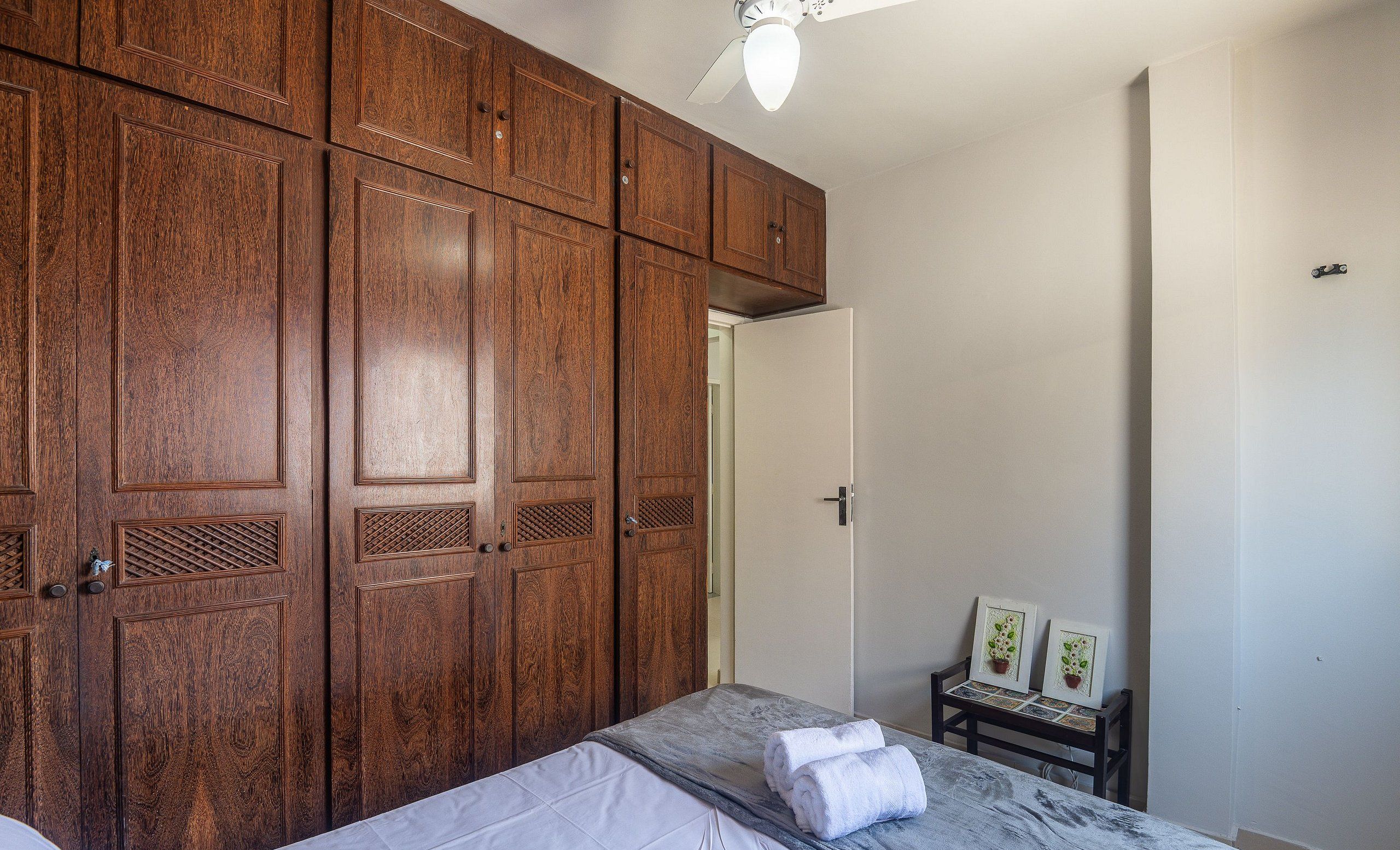 Un dormitorio con un gran armario de madera, una cama con colchón gris y una pequeña mesa con dos cuadros enmarcados.