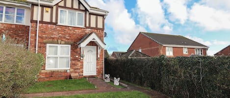 A two-story brick house with a front garden and a hedge.