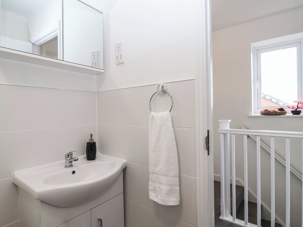 A bathroom with a white sink, a mirror, and a towel hanging on a ring. - The Cosy View (Paignton)
