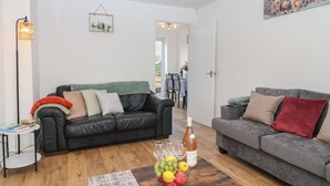 A modern living room with two sofas, a coffee table with fruit and wine, and a dining area in the background. - The Cosy View (Paignton)