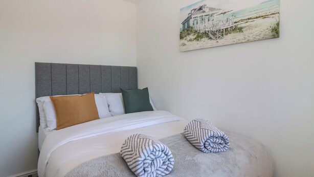 A bedroom with a bed, pillows, and a painting of a beach house. - The Cosy View (Paignton)