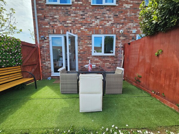 A brick house with a patio, a wooden bench, wicker furniture, and a red fence. - The Cosy View (Paignton)
