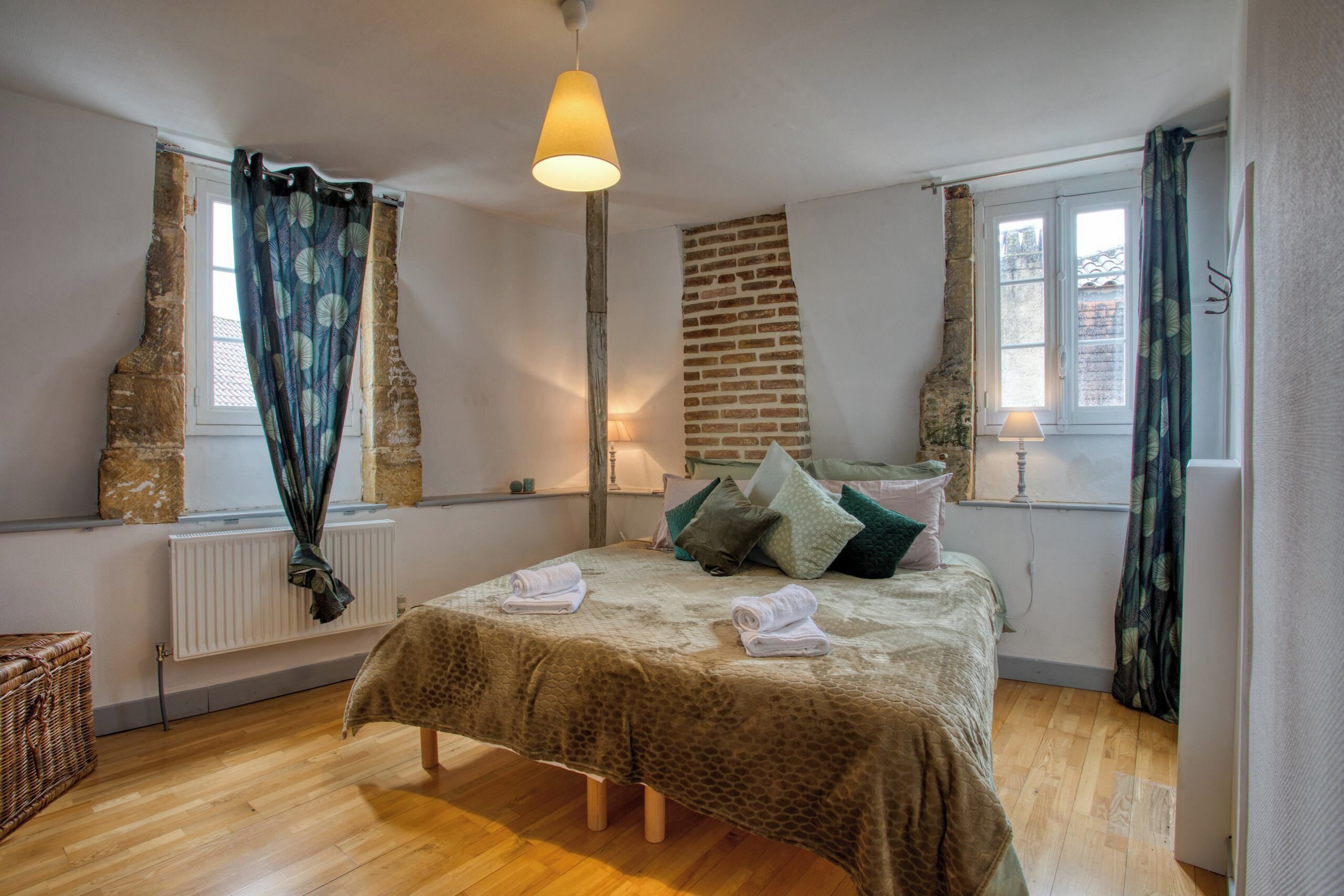 A bedroom with a bed, a radiator, a lamp, and a window with curtains.
