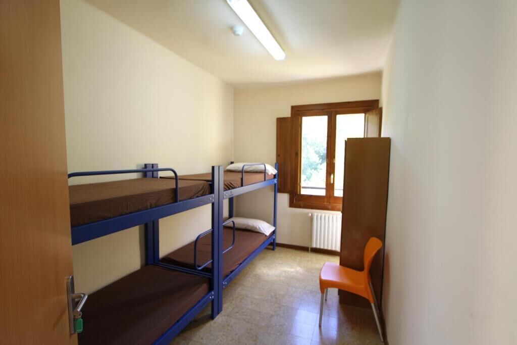 Une chambre de dortoir avec des lits superposés, un radiateur, une fenêtre et une chaise orange.
