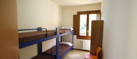 Une chambre de dortoir avec des lits superposés, un radiateur, une fenêtre et une chaise orange.