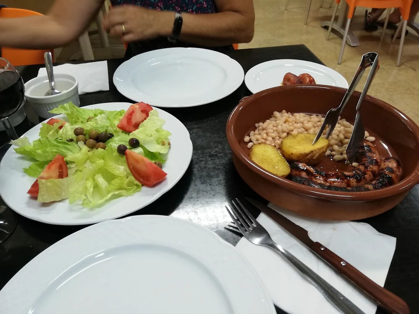 A table with a salad, a bowl of beans and meat, and a wine glass.