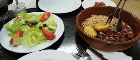 A table with a salad, a bowl of beans and meat, and a wine glass.