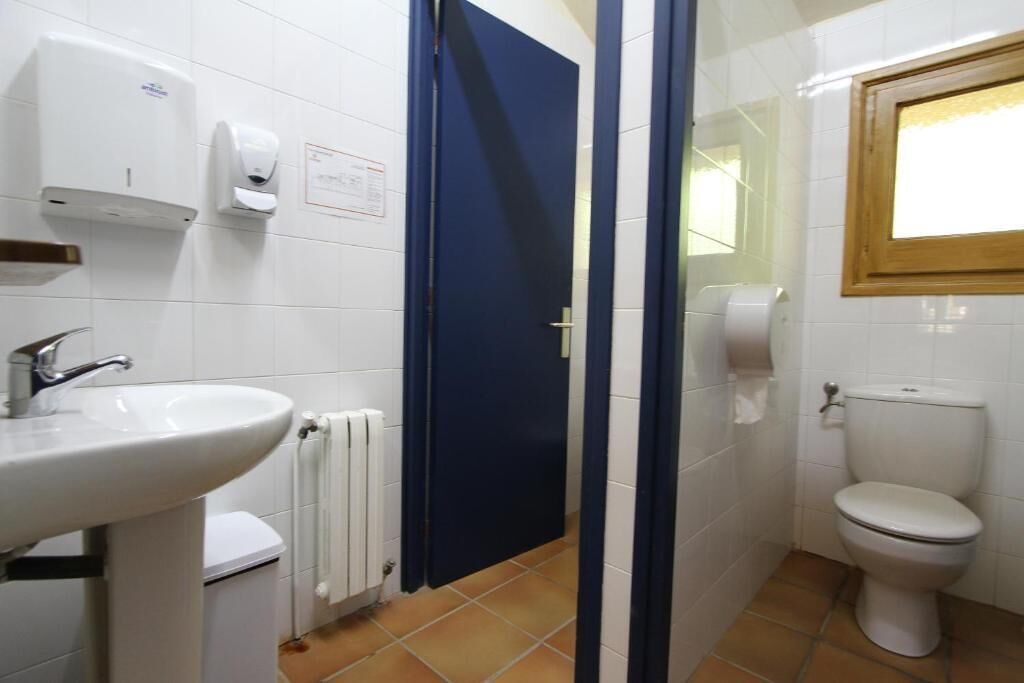 A bathroom with a white sink, a toilet, a blue door, and a window.