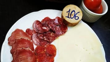A plate with various cured meats and cheese, a wooden number marker, a basket of bread, and a small bowl of tomatoes.